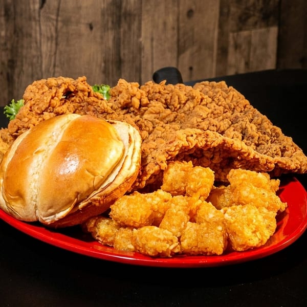 Crispy fried chicken, a bun, and tater tots on a red plate against a dark wood background.